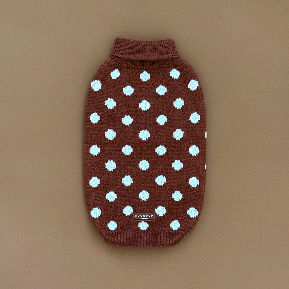 A brown knit dog jumper with pale blue polka dots, on a solid beige background.