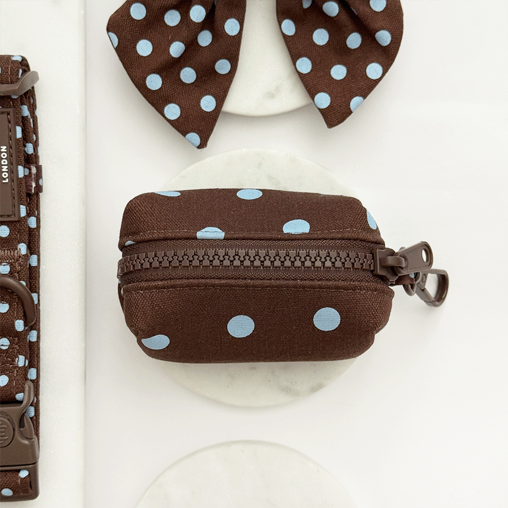 A brown poop bag holder, for dog poo bags, with light blue polka dot design. Featuring brown hardware.