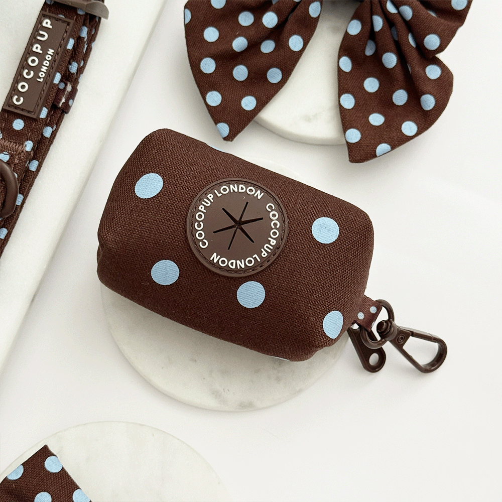 A brown poop bag dispenser, for dog poo bags, with light blue polka dot design. Featuring brown hardware.
