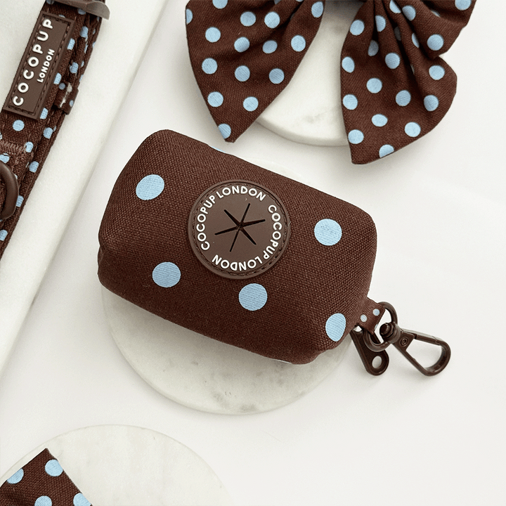 A brown poop bag dispenser, for dog poo bags, with light blue polka dot design. Featuring brown hardware.
