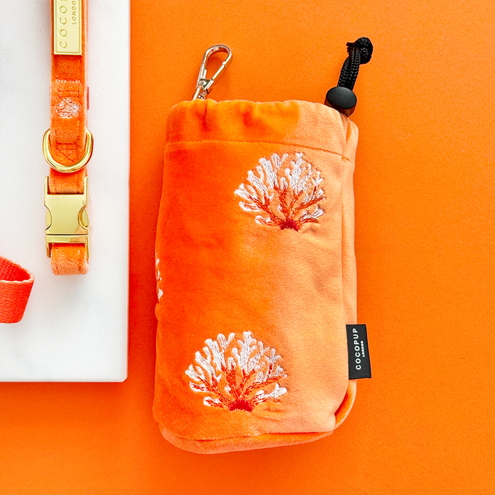 Coral velvet treat pouch and orange dog collar displayed side by side on a white block.