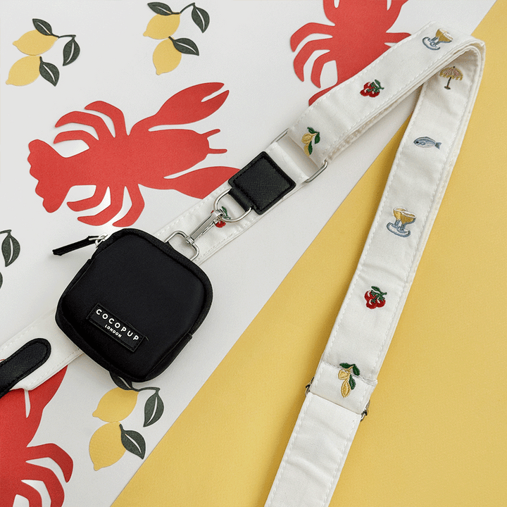 White linen fabric Bag Strap with summer embroidered embellishments. Attached to a black Cocopup Treat Pouch.