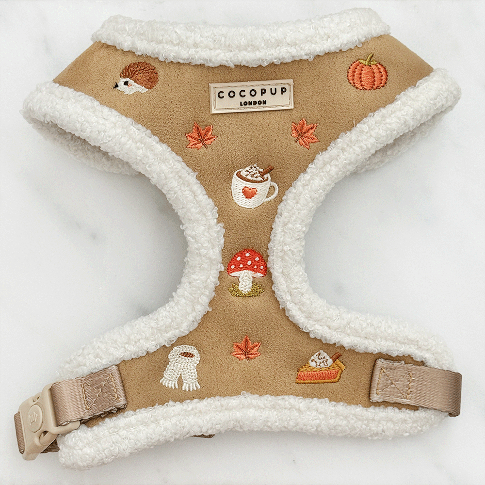 Brown dog harness with white sherpa trim and autumnal-themed embroidery of pumpkins, leaves, a coffee cup, and mushrooms.