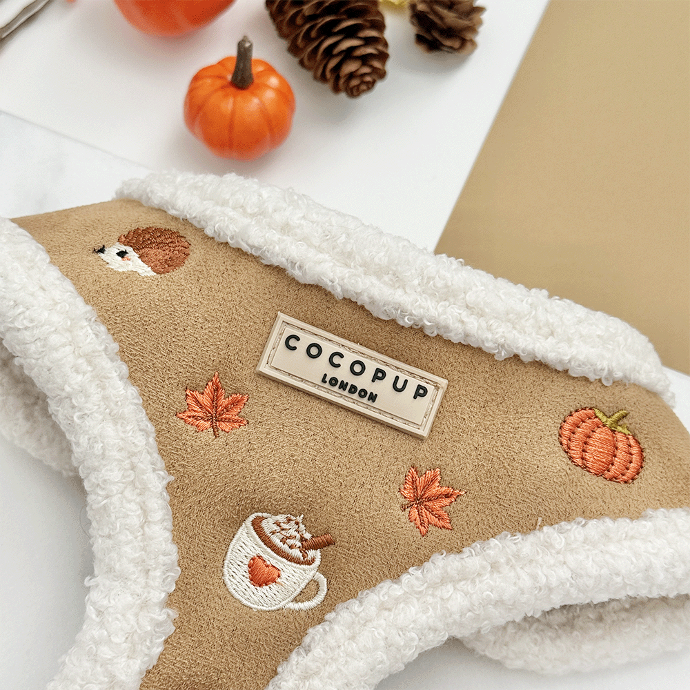 Brown dog harness with white sherpa trim and autumnal-themed embroidery of pumpkins, leaves, a coffee cup, and mushrooms.