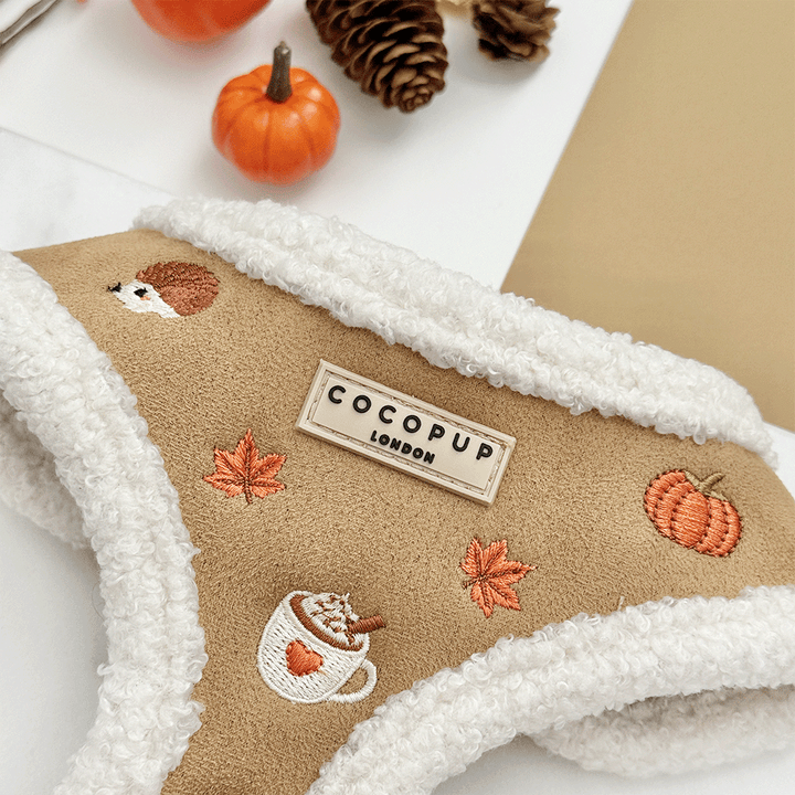 Brown dog harness with white sherpa trim and autumnal-themed embroidery of pumpkins, leaves, a coffee cup, and mushrooms.