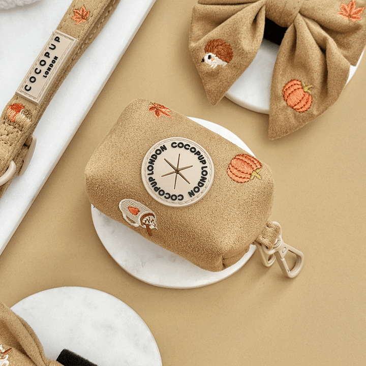 Brown poop bag dispenser, for dog poo bags, with autumnal-themed embroidery of pumpkins, leaves, a coffee cup, and mushrooms.