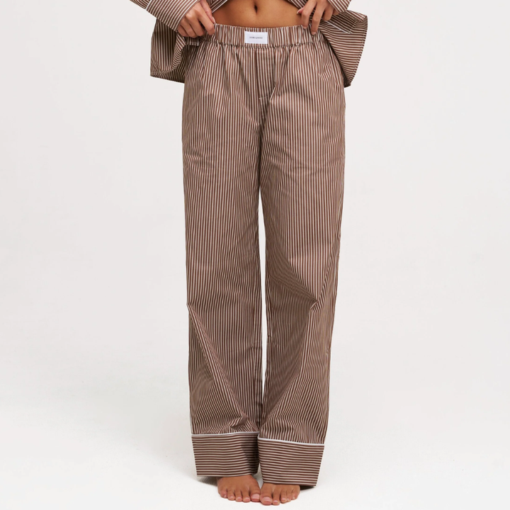 A person wearing loose brown and white vertically striped pajama pants, shown from the waist down against a plain white studio background.