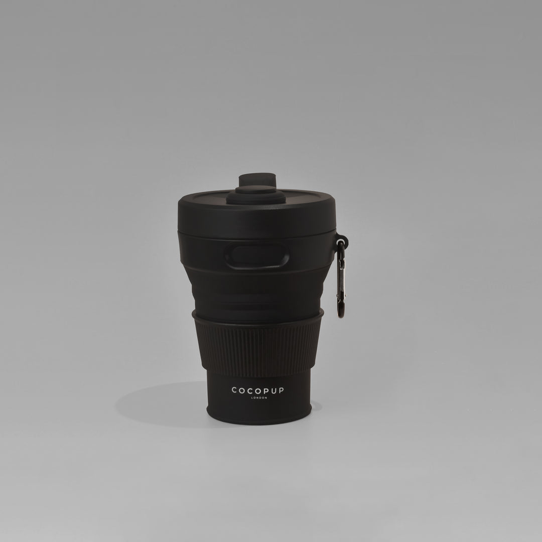 Plain Black Collapsible Silicone Travel Coffee Cup with Cocopup branding and carabiner clip.