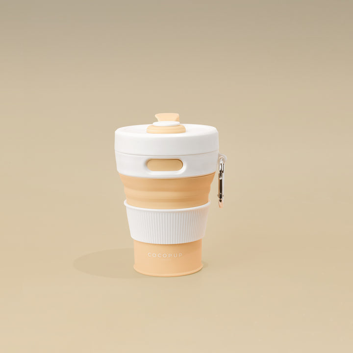 Plain Nude with White Lid Collapsible Silicone Travel Coffee Cup with Cocopup branding and carabiner clip.