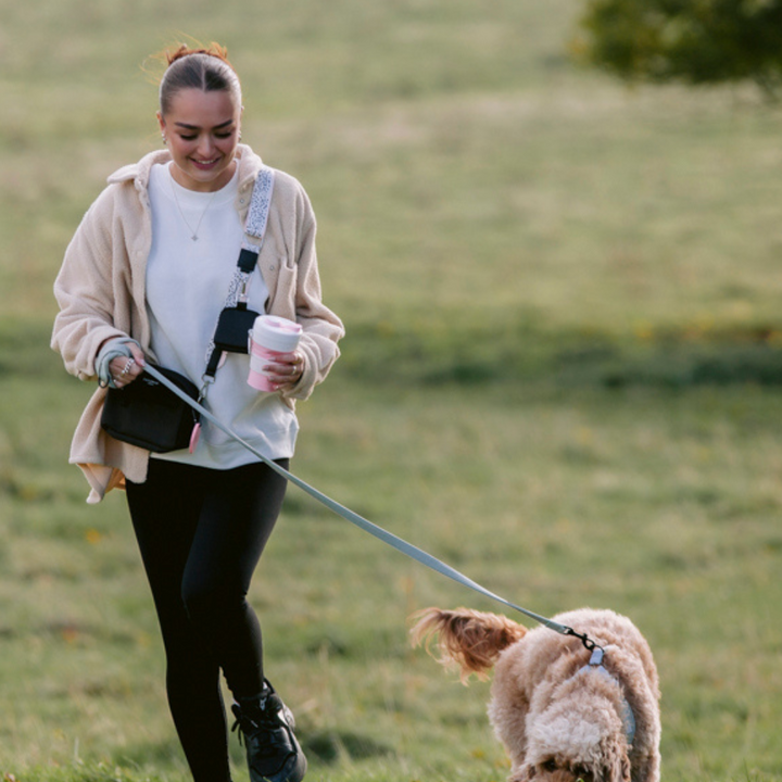 Model walking her dog whilst carrying the Cocopup Pink Coffee Cup wearing the Cocopup Black Dog Walking Bag.