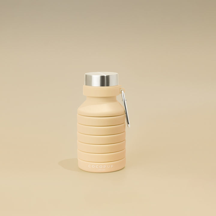Collapsed view of the Plain Nude Silicone Collapsible Water Bottle with Cocopup Branding, Stainless Steel Lid and Carabiner Clip.